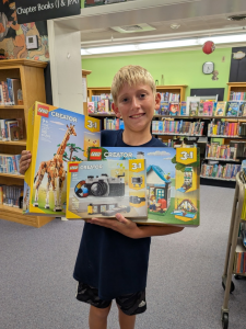 A young boy smiling holding up his prizes for Summer Reading.
