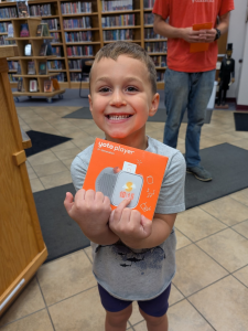 A smiling little boy holding a Yoto player he won as a prize.