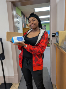 A smiling teen girl holding a projector and speaker she won as prizes.